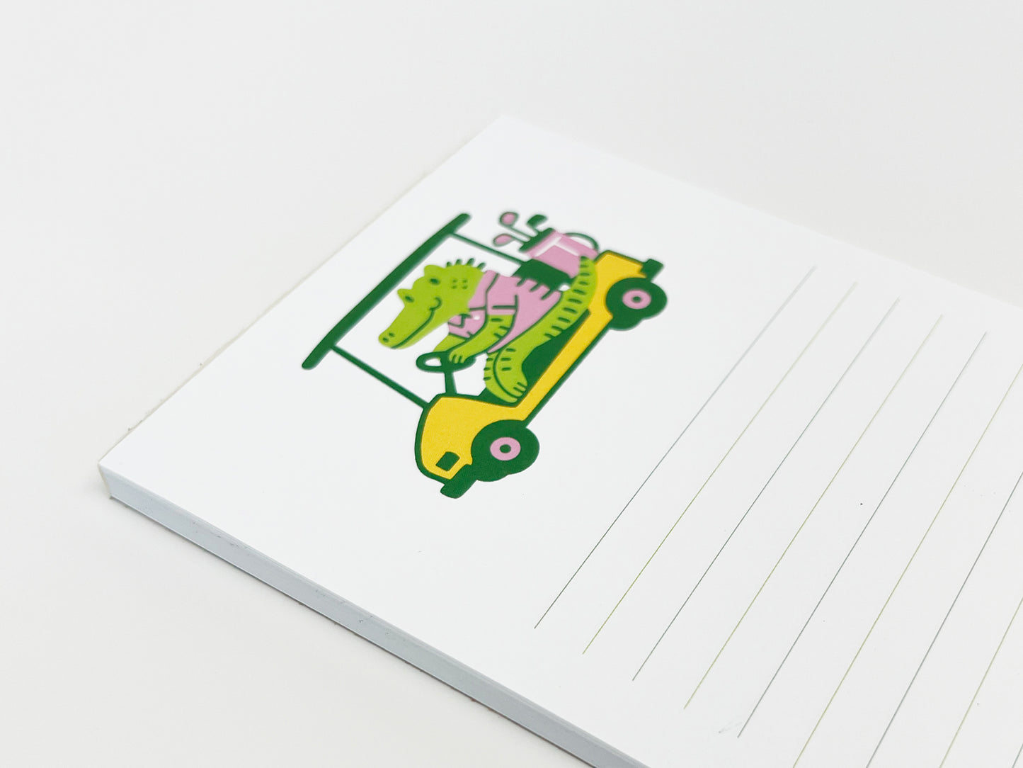 Angled lined notepad with a colorful illustration of an alligator driving a golf cart on a white background.