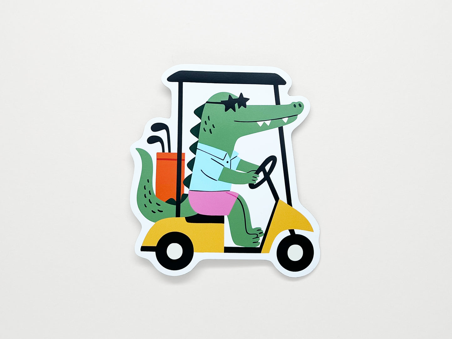 Quirky die-cut magnet of a cartoon alligator driving a yellow golf cart with clubs, funny novelty fridge magnet gift for golfers and golf lovers.