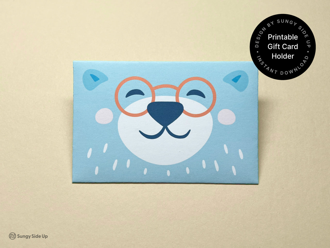 Close-up of the finished printable bear gift card holder showing the front design with a cheerful bear face and orange glasses. The light blue color and friendly illustration make it ideal for kids, teachers, or baby shower gifts. This digital product is an instant download that you can print, cut, and assemble at home to wrap a gift card with extra personality.