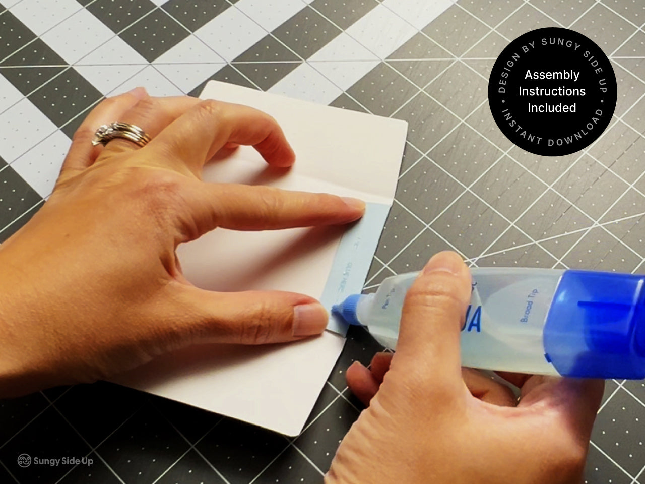Hands applying glue to assemble the printable bear gift card holder on a crafting mat. This step-by-step image shows how easy it is to put together your DIY gift card envelope using the included assembly instructions. Perfect for craft lovers or anyone looking to give a personal, handmade feel to a gift card for birthdays, teachers, or kids.