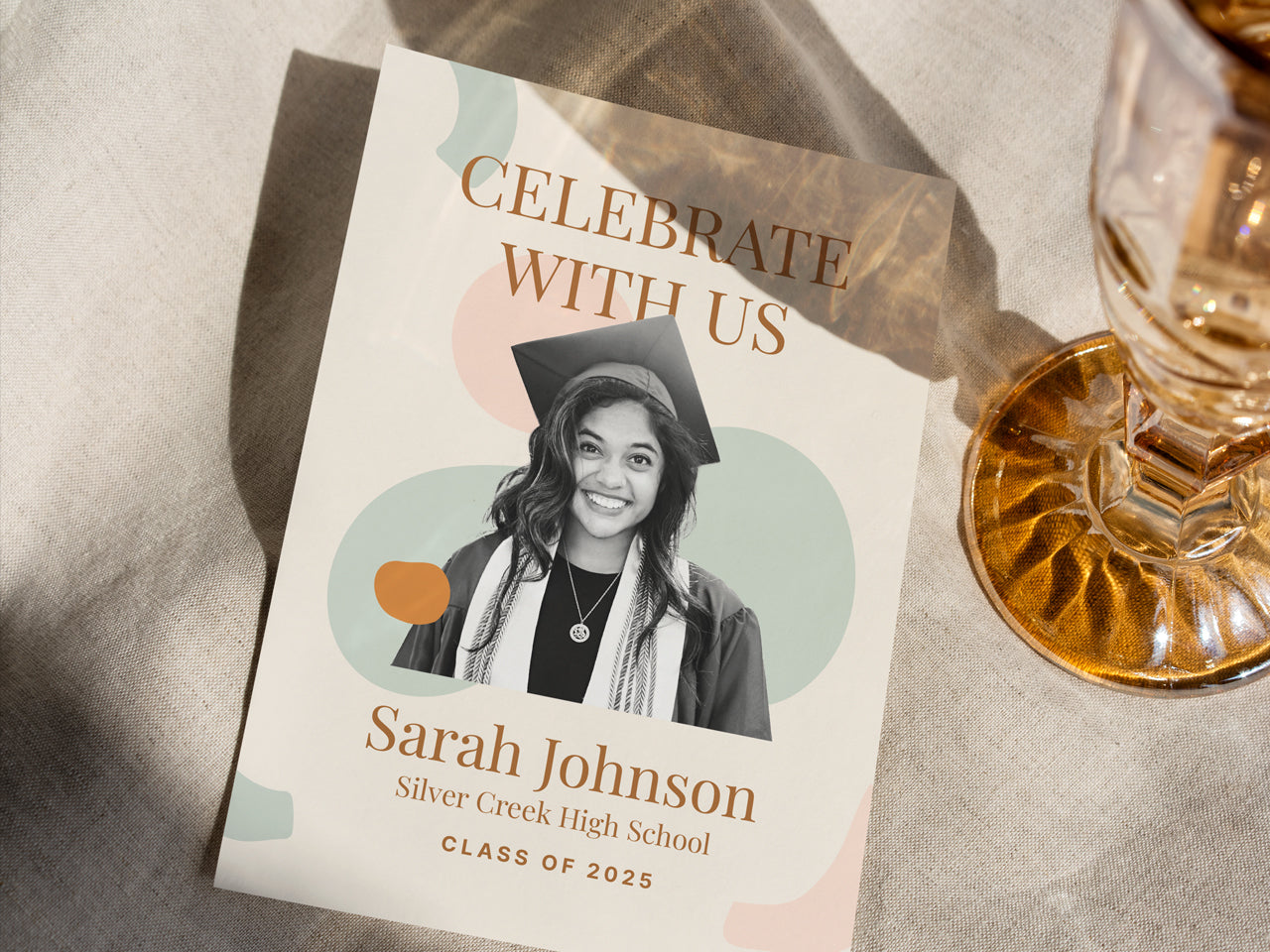 A boho-inspired graduation announcement card with earthy abstract shapes, a personalized graduate photo, and elegant gold-tone serif text. The 5x7 printed grad announcement is styled with champagne glassware and linen fabric, creating a warm, celebratory aesthetic. A perfect custom printed graduation announcement card for high school or college grads, designed to match modern and minimalist grad party themes.