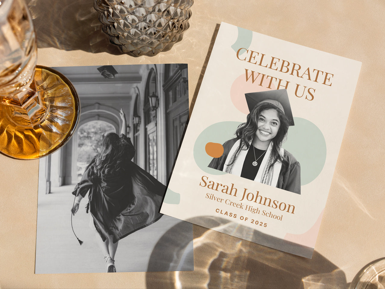 A boho graduation announcement card with a soft, modern abstract design in earthy tones. The 5x7 printed announcement card features a black and white custom photo of a graduate and serif typography, with a matching black-and-white senior portrait in the background. Styled with glassware and warm lighting, this personalized grad announcement card is perfect for high school and college graduates looking for a minimalist, printed graduation card.