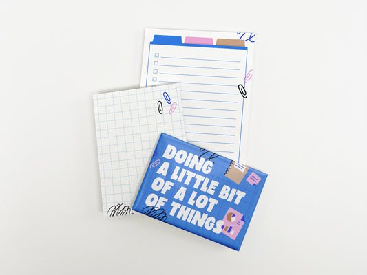 A blue magnet reading "Doing a Little Bit of a Lot of Things" displayed alongside a mini grid notepad and a lined checklist notepad on a white background.