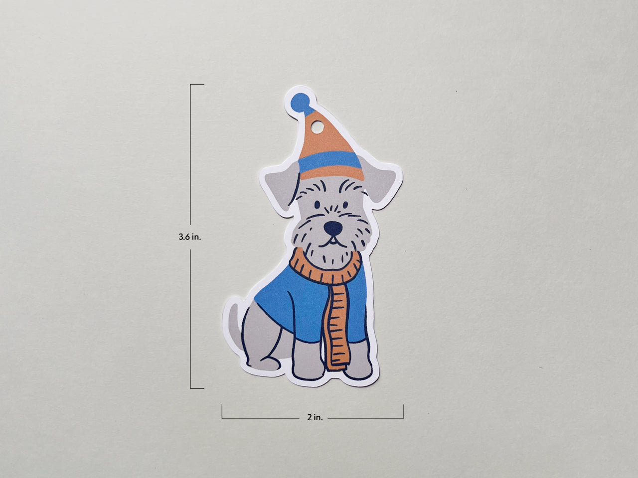Illustrated Schnauzer gift tag featuring a dog in a winter hat and scarf, shown with dimensions. The die-cut tag measures 3.6 inches tall and 2 inches wide, making it ideal for dog lover presents and holiday gift embellishments.