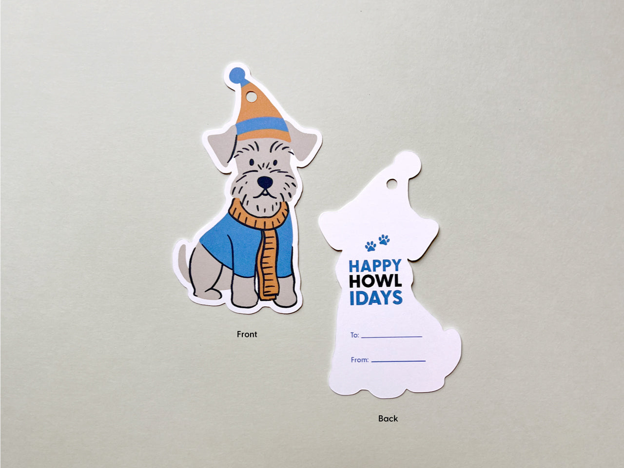 Front and back views of handmade Schnauzer-themed holiday gift tags. The front showcases a cute illustration of a Schnauzer dog in a blue and orange winter hat and scarf, while the back includes the Happy Howlidays greeting with paw print details.