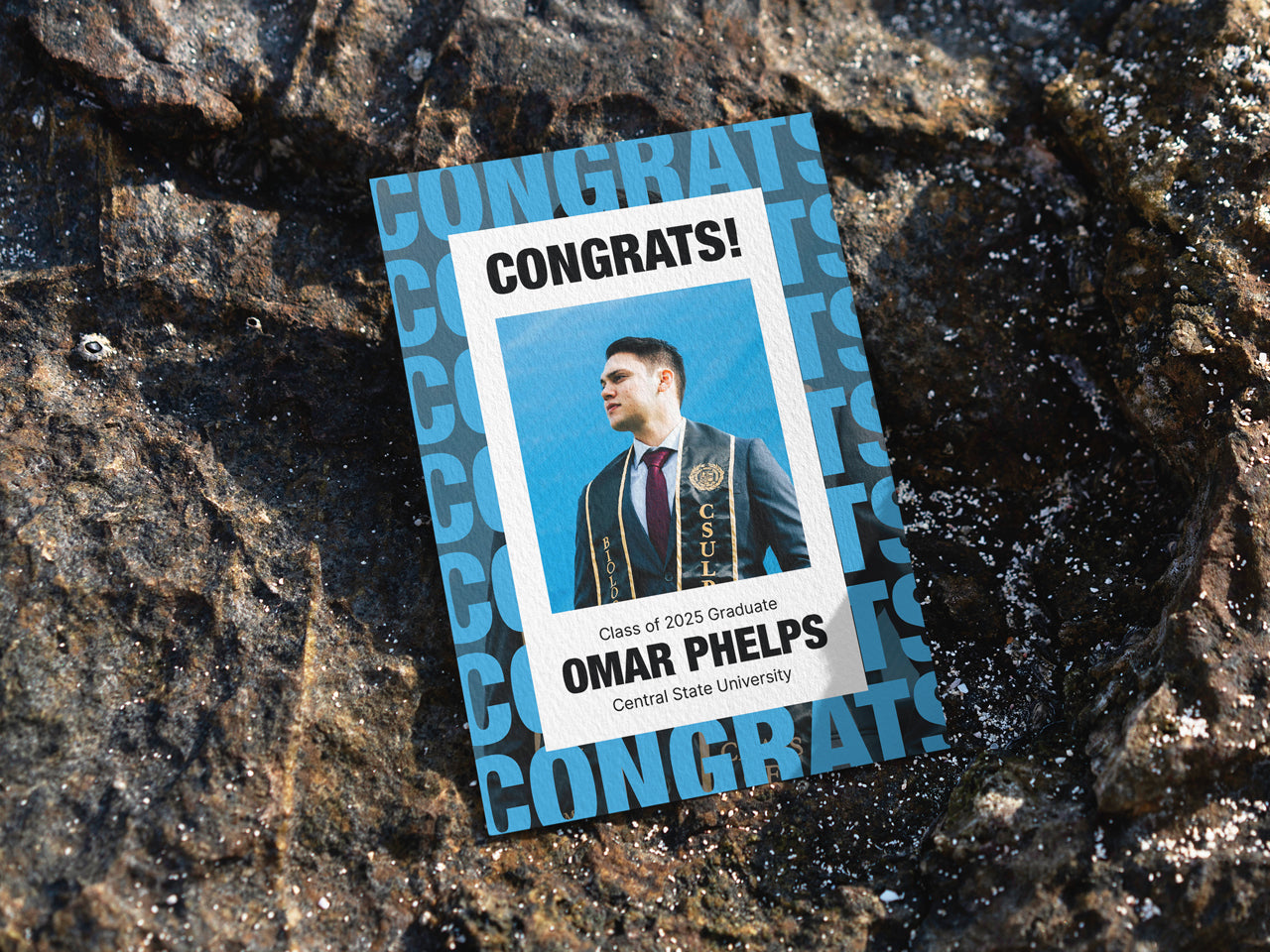 A custom graduation announcement card is placed on a textured surface, emphasizing its bold and modern design. The blue and black text pattern adds a unique touch, making this announcement ideal for graduates who prefer a sleek, minimalistic style. The front of the card showcases a graduate portrait with their name and class year, framed in a simple but impactful layout. For college or high school graduation announcements, this grad card is available with envelope upgrades.