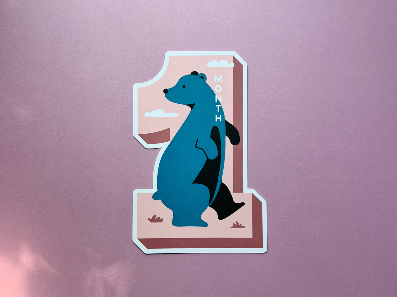 A die-cut milestone card shaped like the number 1. The card features a cute blue-colored bear illustration on a pink background with a modern, minimal design. Perfect for baby's one-month photo props and keepsakes.