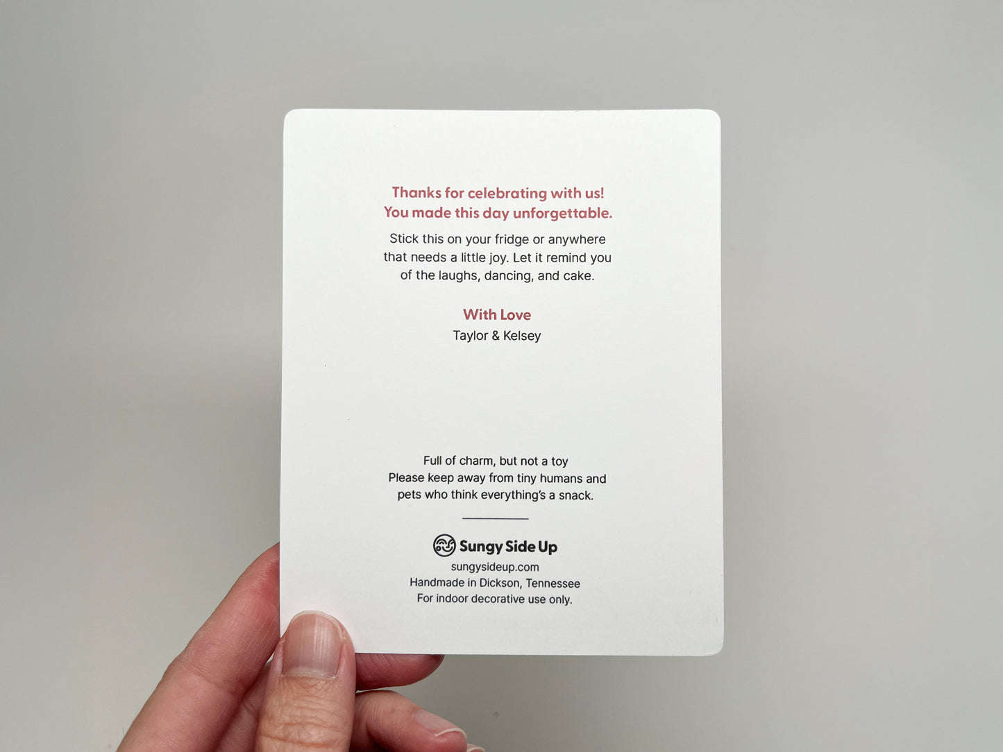 Back of a customizable wedding favor card featuring a thank-you note in red and black text. It thanks guests for celebrating, includes couple names, playful care instructions, and Sungy Side Up branding at the bottom.