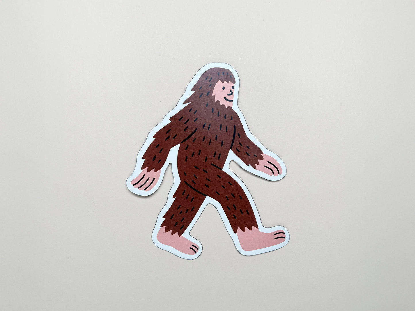 Cute die-cut Sasquatch magnet featuring a smiling brown Bigfoot walking with pink hands and feet; handmade quirky fridge magnet by Sungy Side Up—perfect for whimsical gifts, cryptid collectors, and fun home décor.