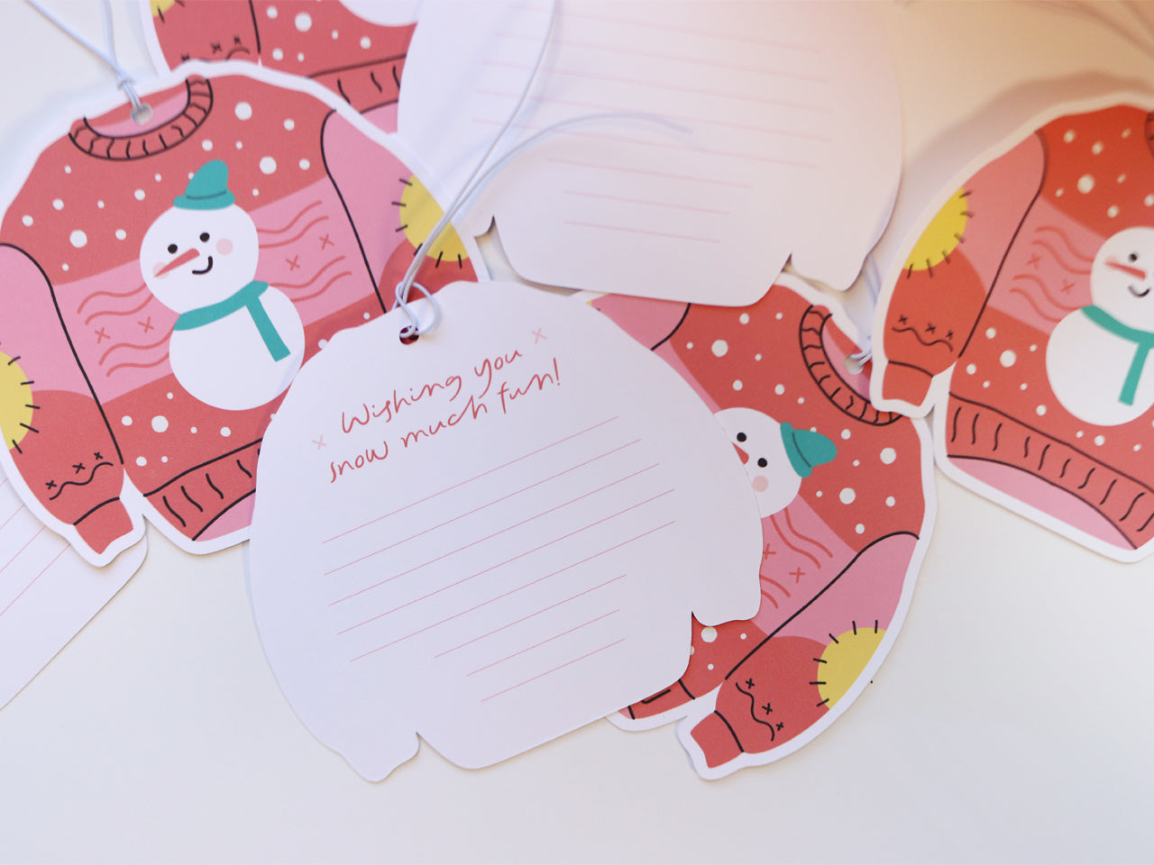 Multiple Christmas sweater-shaped gift tags are displayed, showing the back of some tags, which have a lined space for personalized messages. The phrase “Wishing you snow much fun!” is written on one, adding a charming holiday sentiment.