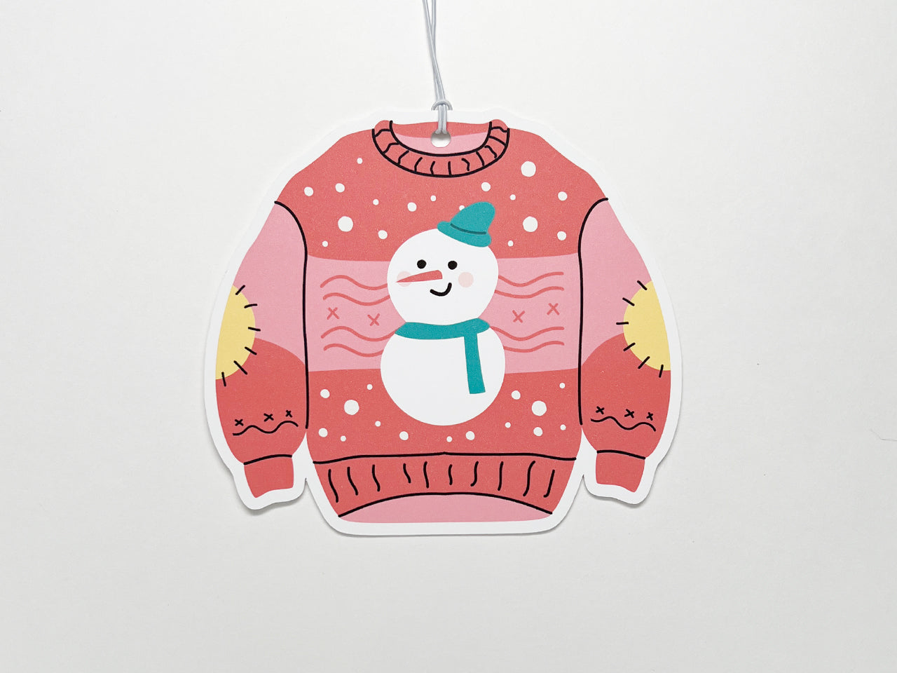 A single pink Christmas sweater-shaped gift tag featuring a smiling snowman with a teal scarf and hat. The whimsical design includes yellow elbow patches and festive snowflakes, making it a fun addition to any holiday gift.