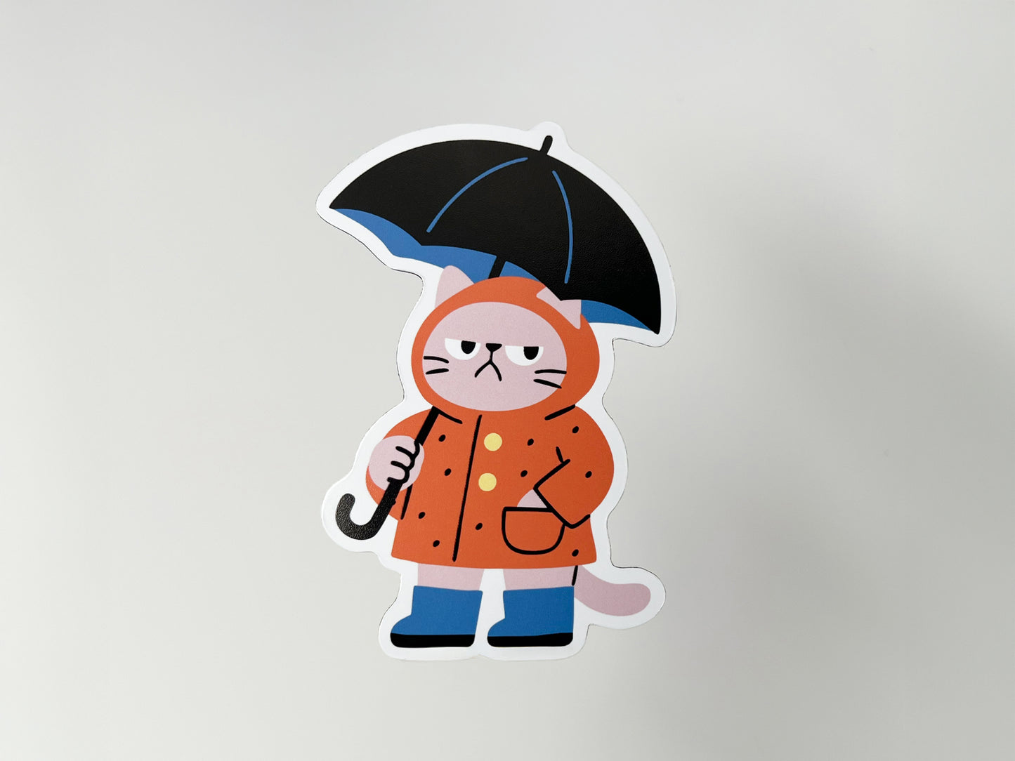 Handmade die-cut magnet of a grumpy cat in orange raincoat with black umbrella, whimsical weather-themed decoration for refrigerators, lockers, or office boards.