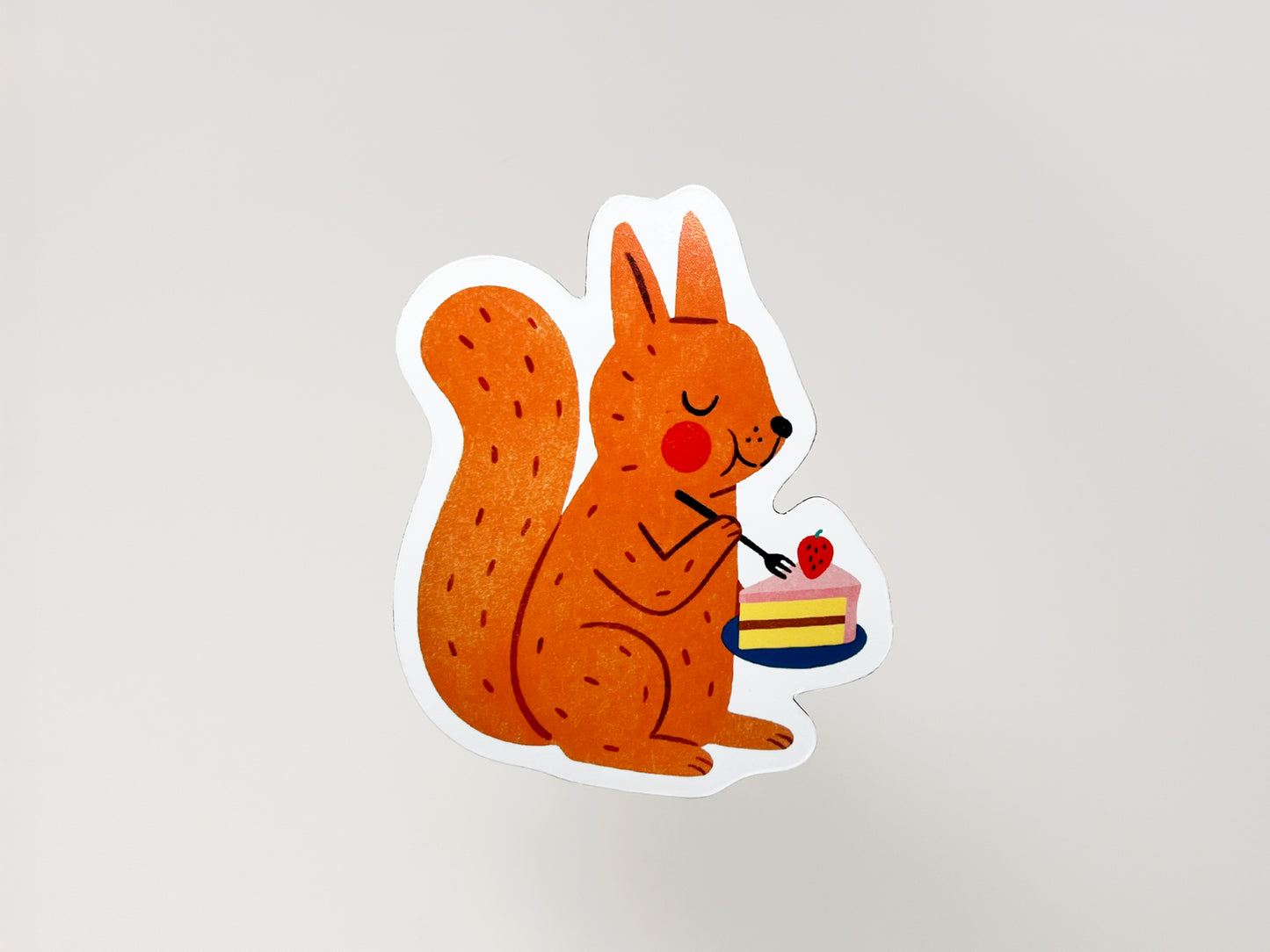Handmade die-cut fridge magnet shaped like a cheerful orange squirrel holding a fork and a plate with a slice of strawberry-topped cake. The cute woodland animal design features bright colors and playful details, perfect for nature lovers, dessert fans, and quirky home decor.