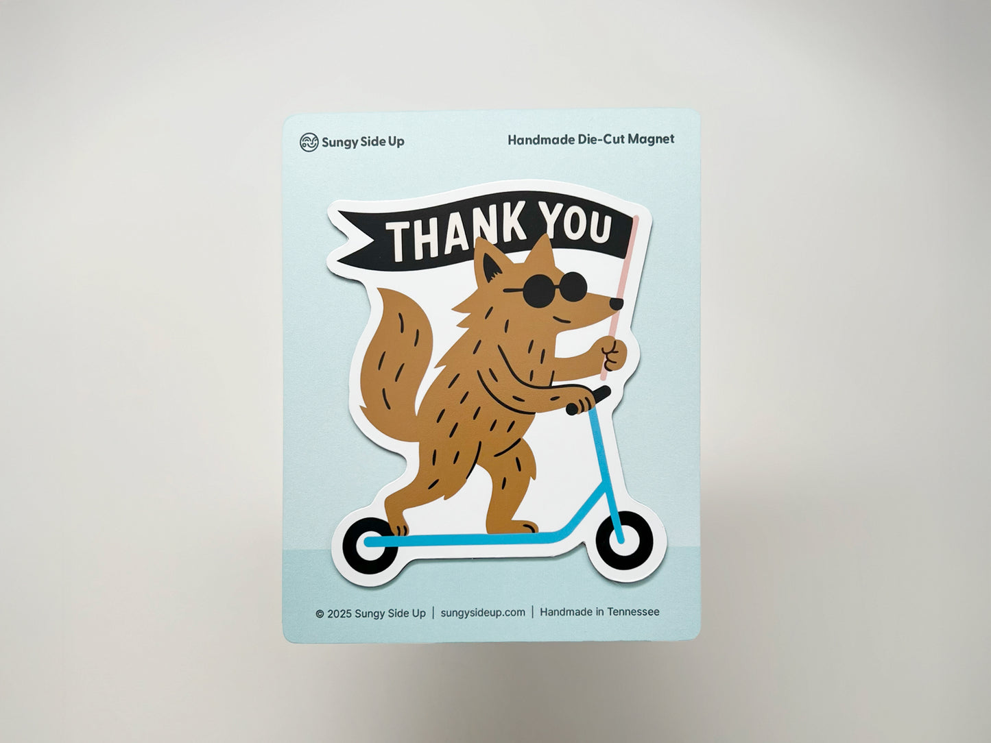 Handmade die-cut magnet featuring a quirky woodland creature on a scooter holding a “THANK YOU” flag. Displayed on branded backing card, this unique fridge magnet makes a fun thank you gift, quirky animal lover present, and playful handmade home décor item.