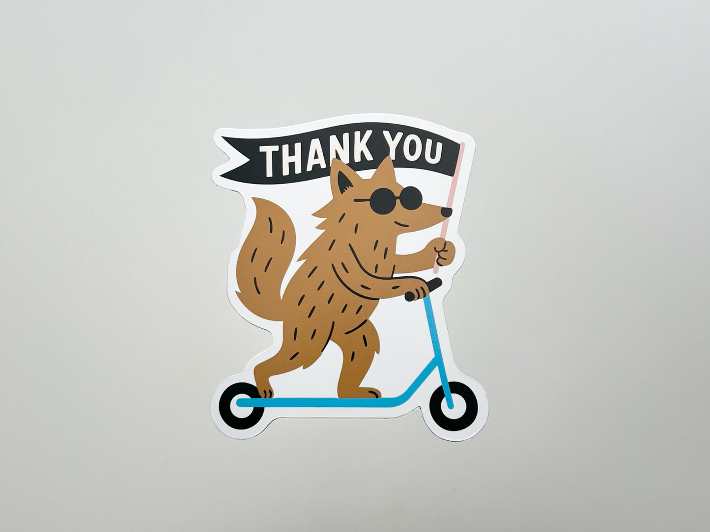 Handmade die-cut magnet featuring a cool brown woodland creature riding a blue scooter and holding a black flag that says “THANK YOU.” Quirky fridge magnet gift, perfect for animal lovers, friends, or coworkers.