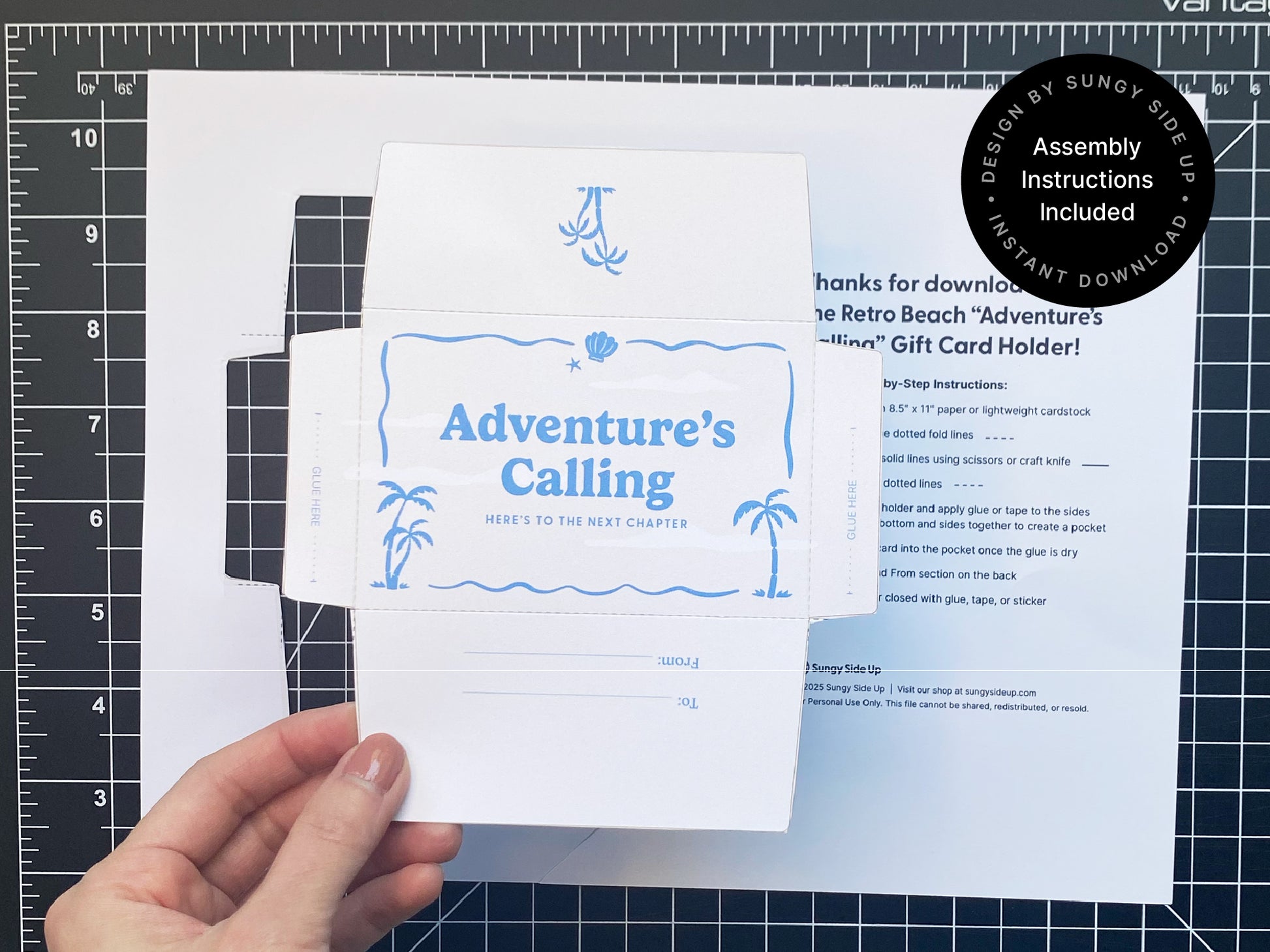 Hand holding a printable retro-style gift card holder with the phrase “Adventure’s Calling” in blue, placed on a black cutting mat. The envelope features palm tree and seashell graphics, and printed instructions are visible in the background. Ideal for DIY crafters, this digital download includes step-by-step directions for assembly. Great for travel-themed gifts, graduations, or farewell celebrations. A creative and nostalgic way to present gift cards for special occasions.
