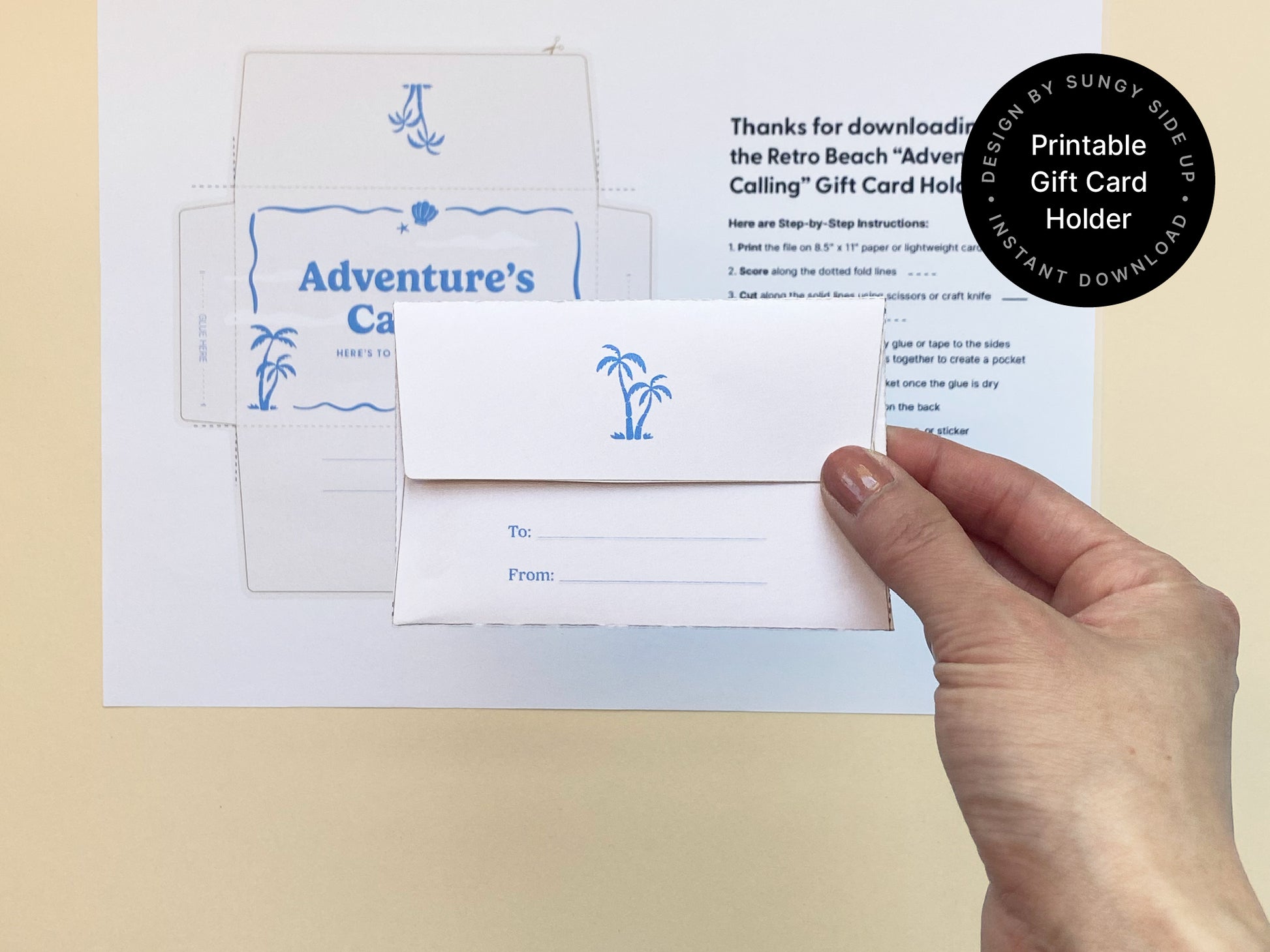 Hand holding the back of a folded printable gift card holder with a retro beach theme. The envelope features a small blue palm tree illustration and "To/From" lines for personalization. Printed instructions and the full design template are visible in the background on off-white paper. Set against a soft beige surface, this DIY gift card holder is ideal for graduations, travel gifts, or farewell occasions. A charming and customizable instant download for creative and meaningful gifting.