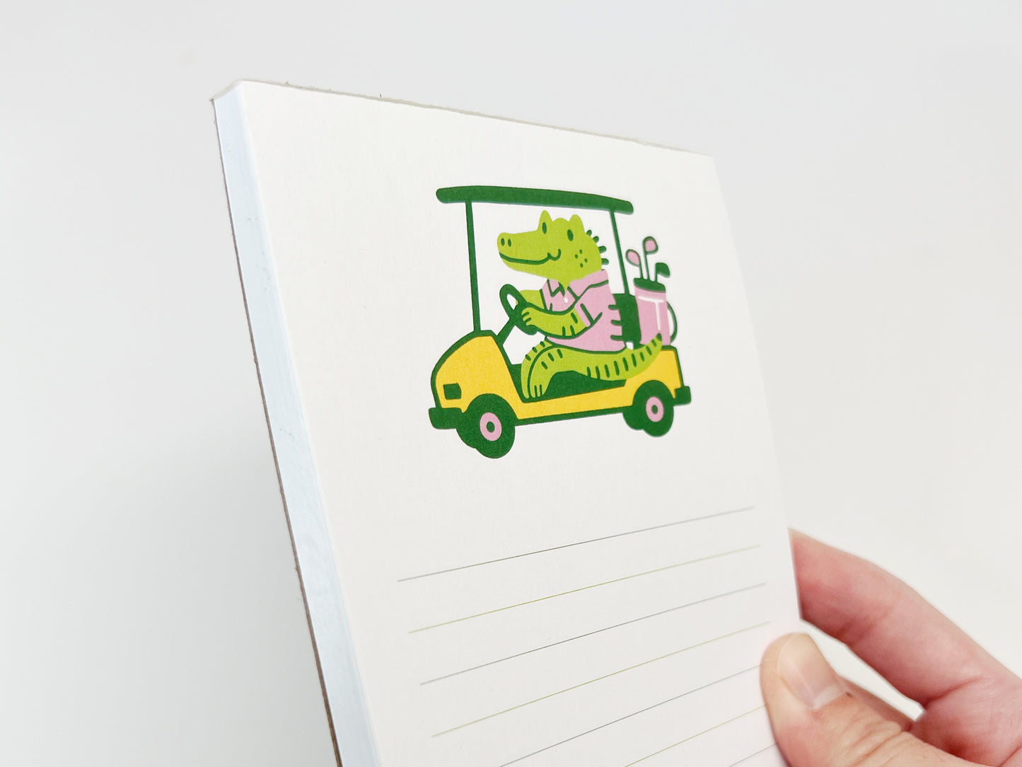 Angled view of a cute alligator golf cart notepad being held, showing the illustrated animal design and lined pages on a small 4.25 x 5.5 inch memo pad.