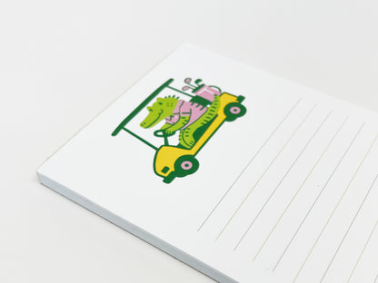 Angled lined notepad with a colorful illustration of an alligator driving a golf cart on a white background.