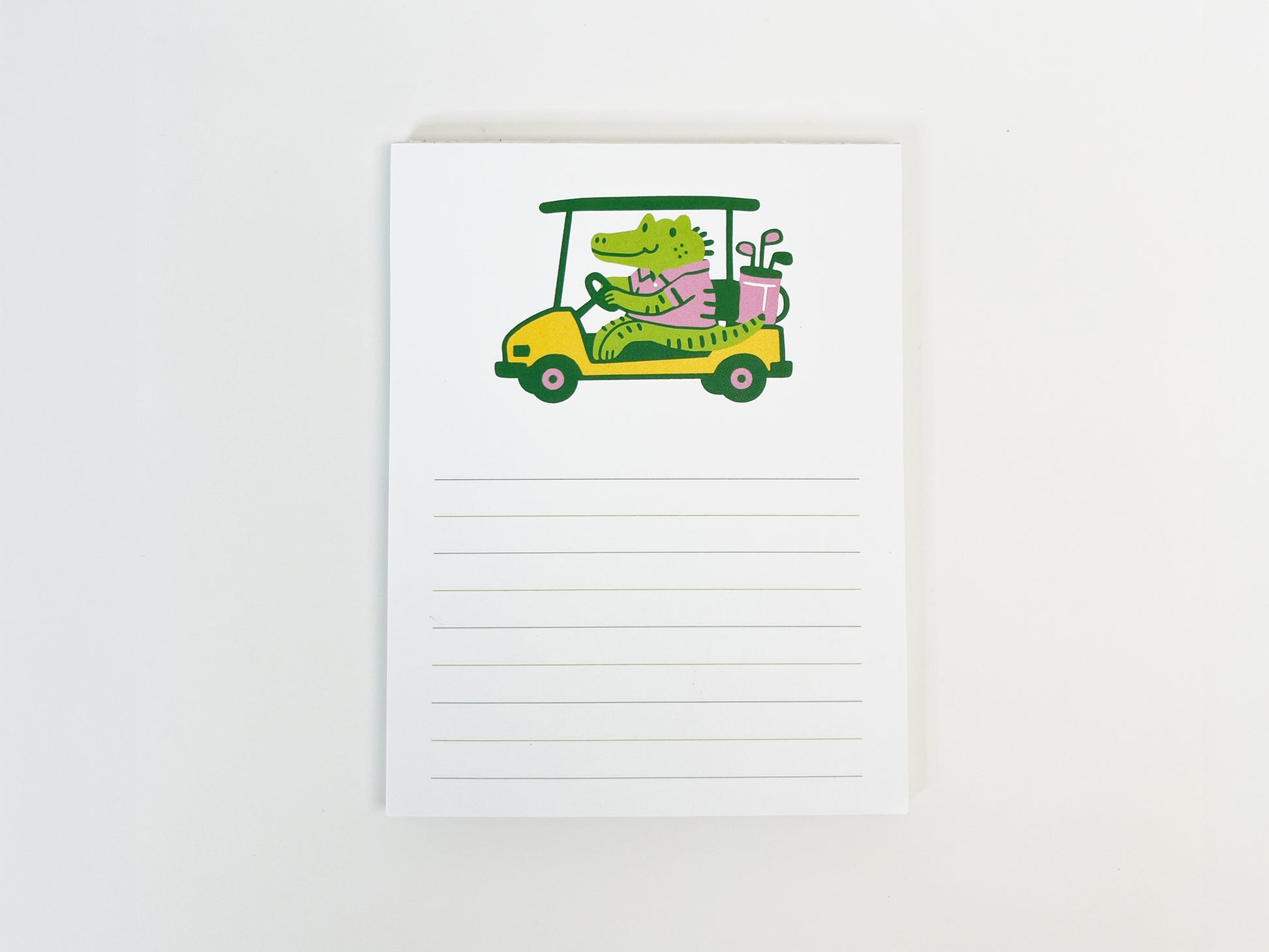 Square lined notepad with a cute illustration of a green alligator driving a yellow golf cart at the top, wearing a pink shirt and carrying golf clubs, with blank writing lines below on a white background.