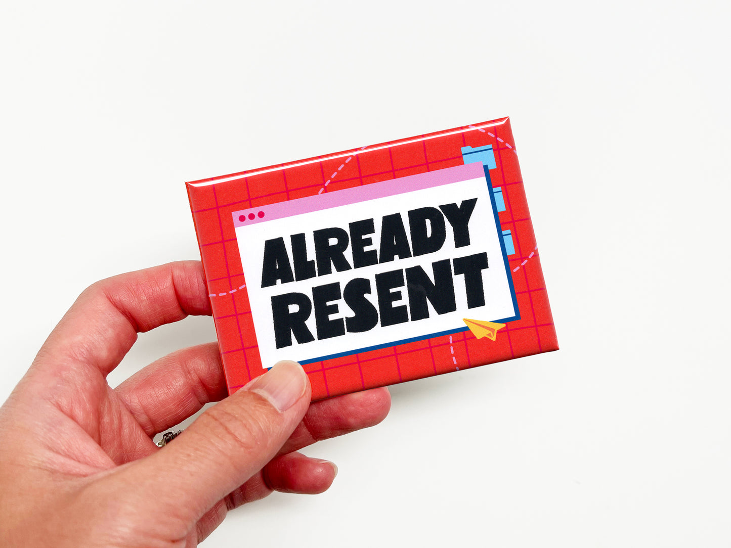Hand holding a funny “Already Resent” office magnet featuring bold black lettering inside a retro email window graphic on a bright red and pink grid background.