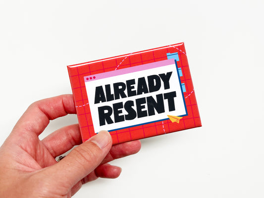 Hand holding a funny “Already Resent” office magnet featuring bold black lettering inside a retro email window graphic on a bright red and pink grid background.
