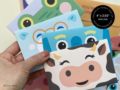 A collection of animal-themed printable gift card holders is shown, featuring designs like a winking cow, a frog with wide yellow eyes, and a blue elephant with playful details. The envelopes are colorful, sized at approximately 4" x 2.63" when folded, and designed for easy assembly at home. A hand holds some of the assembled gift card holders, highlighting their vibrant colors and cute expressions. These printables are ideal for kids’ birthdays, parties, and creative gifting.