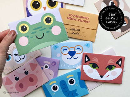 A variety of printable animal-themed gift card holders are displayed, featuring colorful, cartoon-like animal faces including a frog, fox, owl, pig, and sloth. A hand holds a frog card holder up close, showing its cute design with large yellow eyes and pink cheeks. These gift card holders are part of a 12-design bundle and can be cut, folded, and assembled at home, offering a fun and creative way to present gift cards for kids' parties, birthdays, and holidays.