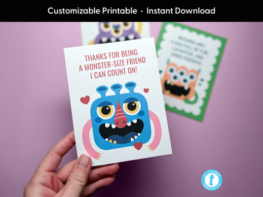 Hand holding a colorful printable card featuring a blue cartoon monster with yellow eyes, a pink nose, and arms. The card reads, Thanks for being a monster-size friend I can count on! Two additional monster-themed cards are in the background,