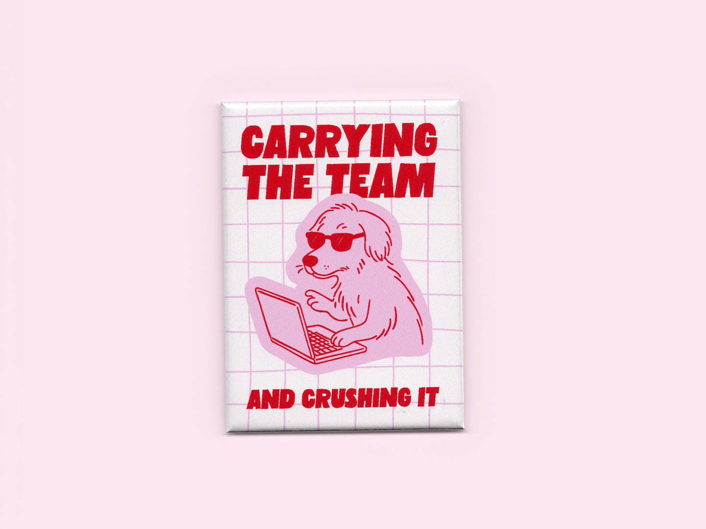 Pink and white rectangular magnet featuring bold red text that says “Carrying the Team and Crushing It” with an illustration of a dog wearing sunglasses while working on a laptop over a light pink grid background.