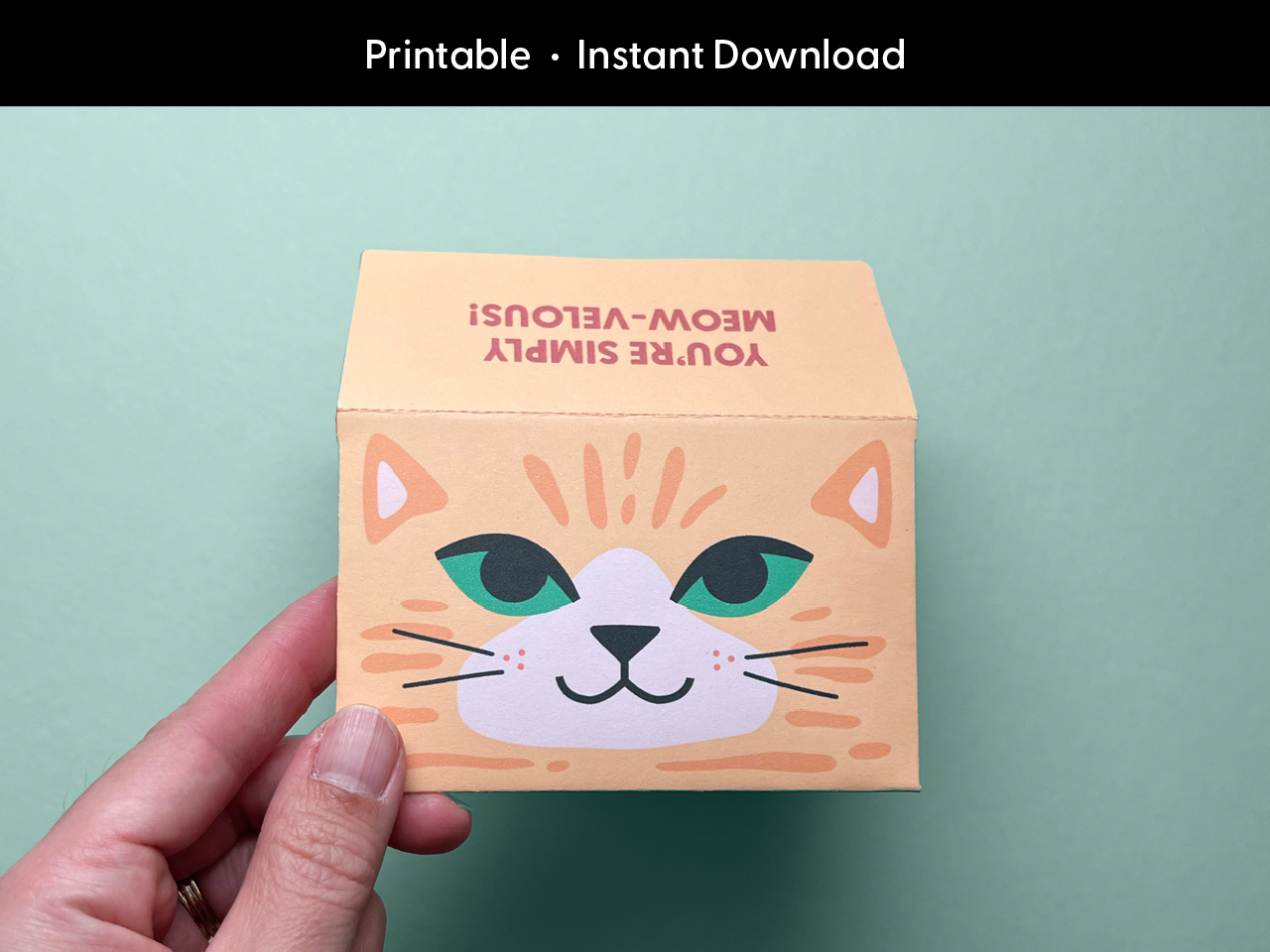 A hand holds the completed printable cat gift card holder with a fun orange tabby cat face and the phrase “You’re Simply Meow-velous!” on the folded flap. The text “Printable • Instant Download” is written at the top of the image. Perfect for birthdays, teacher appreciation, and thoughtful thank-you gifts, this DIY envelope template is easy to print and assemble at home. Designed by Sungy Side Up for creative gifting.