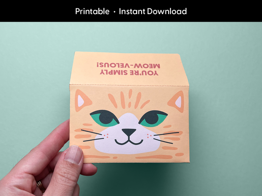 A hand holds the completed printable cat gift card holder with a fun orange tabby cat face and the phrase “You’re Simply Meow-velous!” on the folded flap. The text “Printable • Instant Download” is written at the top of the image. Perfect for birthdays, teacher appreciation, and thoughtful thank-you gifts, this DIY envelope template is easy to print and assemble at home. Designed by Sungy Side Up for creative gifting.