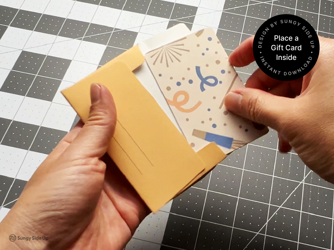 A hand places a colorful gift card into the back of a printable envelope made from peach-colored paper. The folded holder shows the “To” and “From” lines clearly, ready to be filled out. Set on a craft mat background, this image highlights the functional use of the envelope and how it securely holds a standard gift card. Perfect for DIY gifts, teacher appreciation, and party favors using this instant digital download.