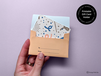 A hand displays the finished cat-themed printable gift card holder with a gift card partially inserted. The envelope features neat “To” and “From” lines on the back and is set against a soft purple background. This image shows how the envelope works as a functional and creative wrapping for standard-sized gift cards. It’s ideal for thank-you notes, birthdays, and small tokens of appreciation.