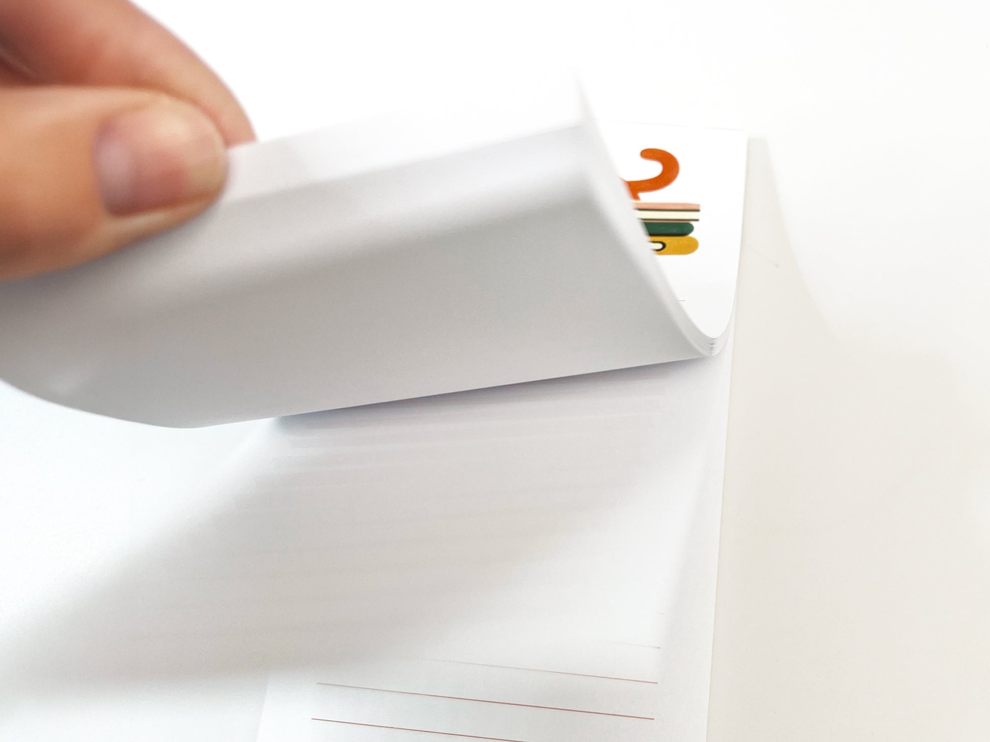 Close-up of a hand flipping through the pages of a slim lined notepad, showing the thickness of the paper and the illustrated cat reading design visible on the top page.