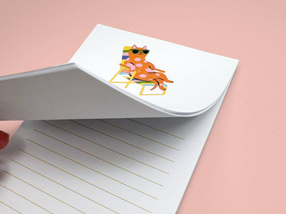 Close-up of a 4x6 lined notepad with the top sheet partially lifted to show the thickness of the paper stack. The notepad features a playful illustration of a pink polka-dot cat wearing green sunglasses while lounging on a rainbow-striped beach chair. Light yellow writing lines appear on each page. The image highlights the quality and thickness of the 50-sheet memo pad, perfect for desk notes, reminders, or gifts for cat lovers.