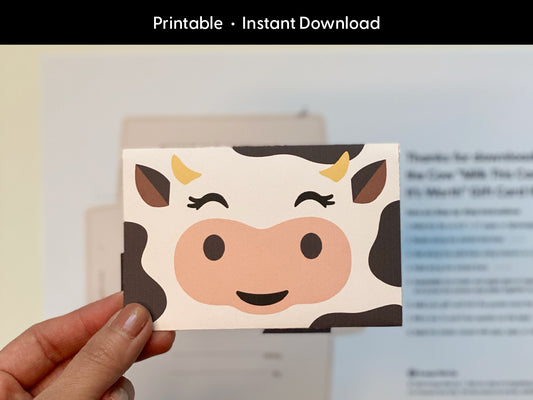 Hand holding an assembled printable cow gift card holder featuring a cute cartoon cow face, with blurred instructions in the background. This digital download template is perfect for gifting teachers, kids, or friends during birthdays, baby showers, or holidays. Designed for easy at-home crafting, this DIY cow envelope adds a fun farm animal twist to personalized gift card giving. Instant download for quick use.
