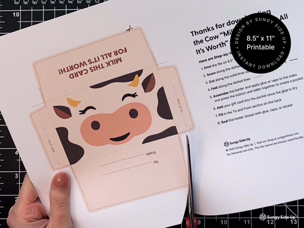Hand holding a printed 8.5 by 11 inch sheet featuring a cow gift card holder template and assembly instructions. The cutout design includes a cute cow face and To and From section. This printable envelope is a digital download for crafting unique gift card holders at home. Perfect for birthdays, teacher appreciation, baby showers, and party favors. Designed for budget-friendly DIY gifting with a farm animal theme.