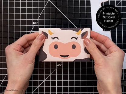 Hands holding a finished printable cow gift card holder with a cute cow face design on the front. This DIY gift card envelope is ideal for birthdays, teacher appreciation, or baby shower favors. Printed and assembled at home, the cardholder adds a fun farm animal theme to your gift presentation. This instant download template is perfect for anyone who loves crafting unique and memorable gift card packaging.