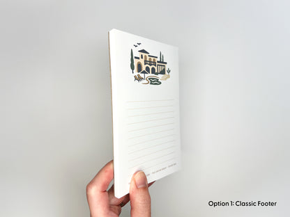 Side view of personalized 4x6 real estate notepad showing paper thickness, Mediterranean-style home illustration, and lined writing space for custom realtor stationery and closing gifts.