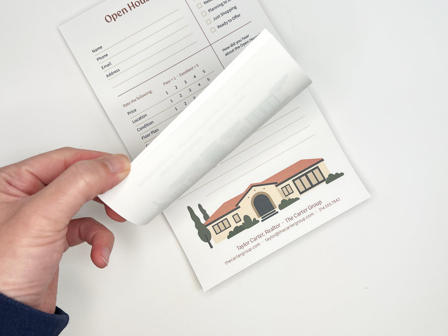 Hand flipping a page of a custom 5 × 8 Open House Feedback real estate notepad, revealing tear-off sheets with structured buyer feedback sections and a customizable branded footer featuring agent contact information and an illustrated home graphic.