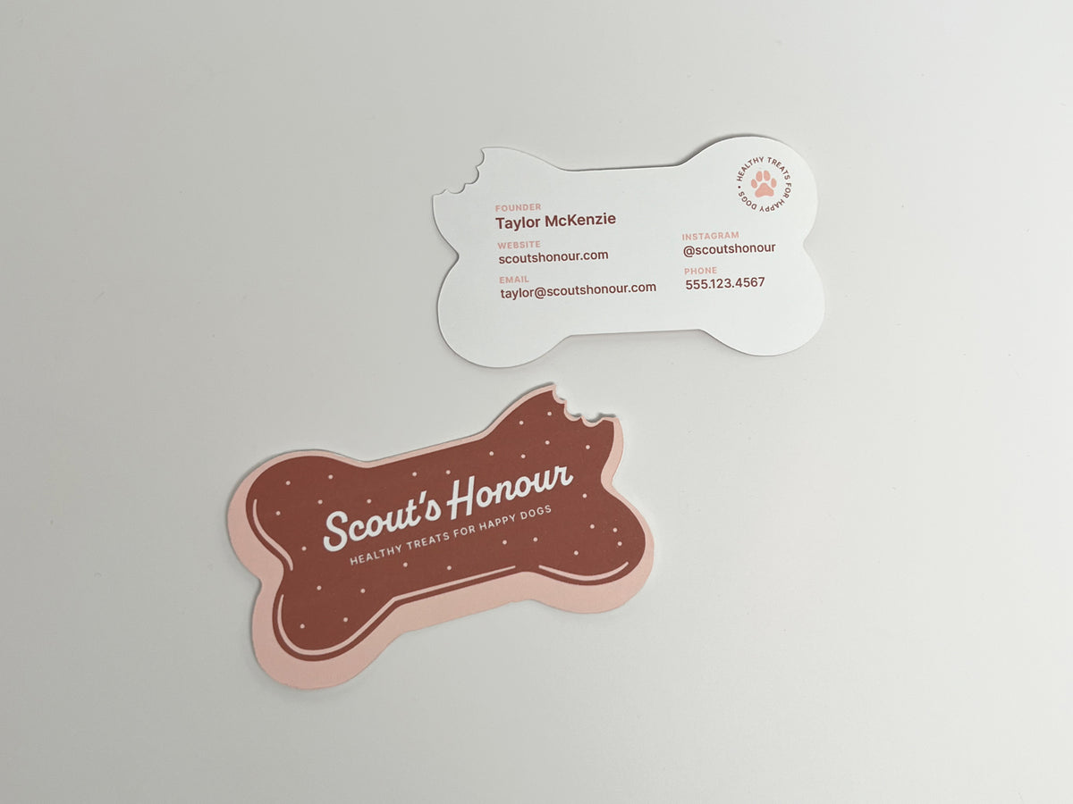 Front and back of a bitten, bone-shaped dog bakery business card featuring a brown treat design and editable contact information.