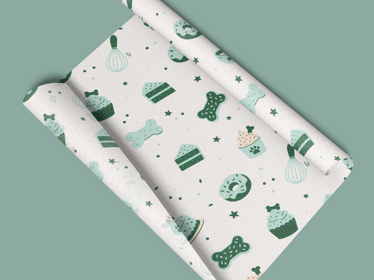 Seamless dog bakery pattern in the white colorway, shown on a sheet of tissue paper rolled at both ends on a sage green background. The design features bone-shaped cookies, bone-topped cupcakes, cake slices, donuts, whisks, and stars in mint and dark green.