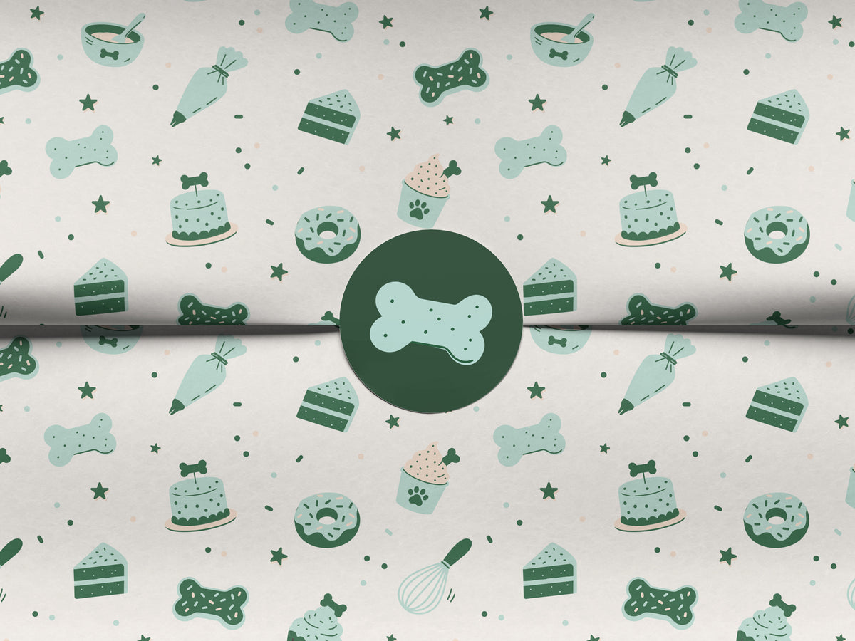 Seamless dog bakery pattern in the white colorway, shown on folded tissue paper sealed with a round dark green sticker featuring a mint bone-shaped cookie. The repeating design shows bone cookies, bone-topped cakes, paw-print cupcakes, cake slices, donuts, piping bags, treat bowls, whisks, and stars in mint and dark green.