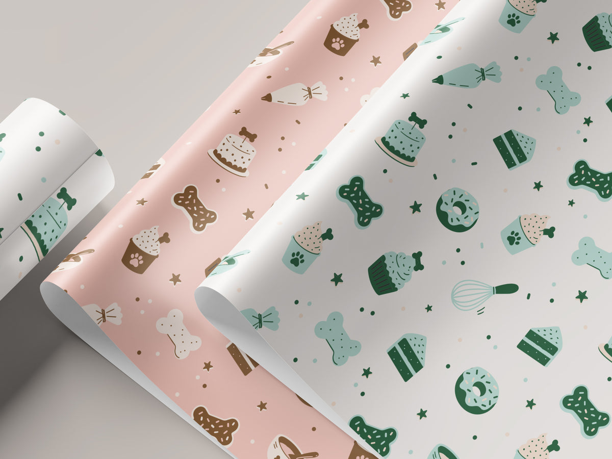 Seamless dog bakery pattern shown on unrolled pink and white wrapping paper. The design features bone-shaped cookies, bone-topped cakes, paw-print cupcakes, donuts, piping bags, a whisk, and stars in mint, green, and brown.