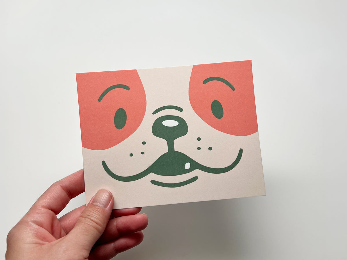 A hand holding a minimalist illustration of a dog's face against a plain white background.