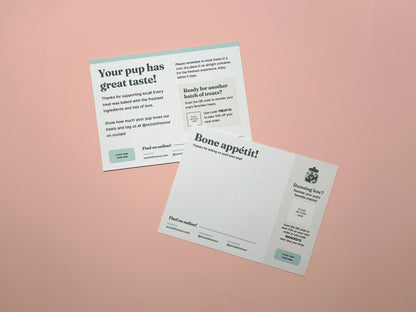 Two back layouts of printed pet treat cards or postcards laid on a soft pink background. One card reads 'Your pup has great taste!' and the other reads 'Bone appetit!'.