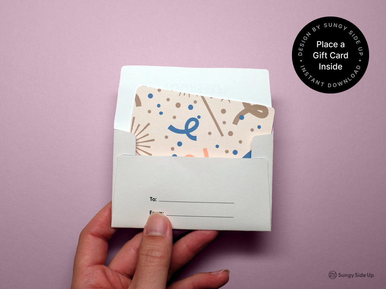 Hand holding an assembled printable dog gift card holder with a colorful card partially inserted inside. The envelope is white with lines labeled To and From on the back flap. A round black label on the right reads Place a Gift Card Inside and includes branding for Sungy Side Up. The background is soft pink, giving the image a clean and cheerful look for digital product listing use.
