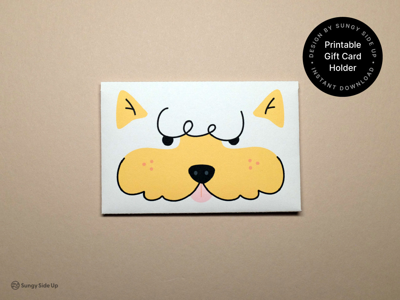Flat lay photo of the completed printable gift card holder featuring a cute cartoon dog face in yellow and black with curly eyebrows and a black nose. The envelope is centered on a light beige background. A circular label on the top right reads Printable Gift Card Holder and mentions Instant Download and Designed by Sungy Side Up. This image highlights the front design of the finished product.
