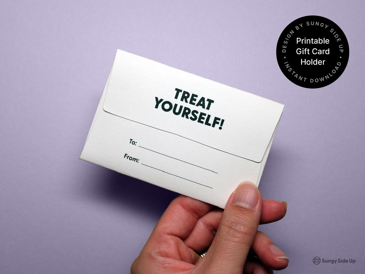 Hand holding the back of the completed printable dog gift card holder on a purple background. The back flap shows the phrase Treat Yourself in bold uppercase letters, with labeled lines for To and From. A round black label in the top right highlights Printable Gift Card Holder and Instant Download with the Sungy Side Up brand. The photo emphasizes the back design and customization features.